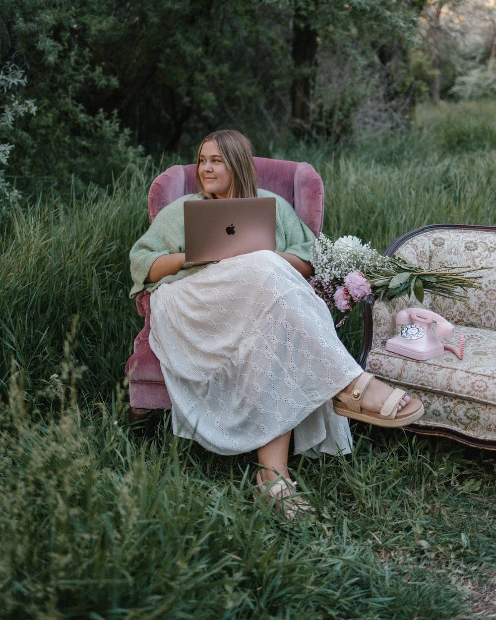 Sydnee editing on a laptop in a pink armchair